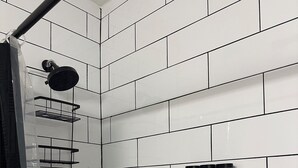A bathroom with white subway tiles, a shower with a black curtain, and two bottles of shampoo and conditioner on the wall. - Stylish Apt: 20 Min to Manhattan, Groups (West New York)
