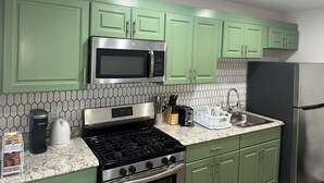 A kitchen with green cabinets, a stainless steel microwave, a gas stove, a coffee maker, and a refrigerator. - Stylish Apt: 20 Min to Manhattan, Groups (West New York)