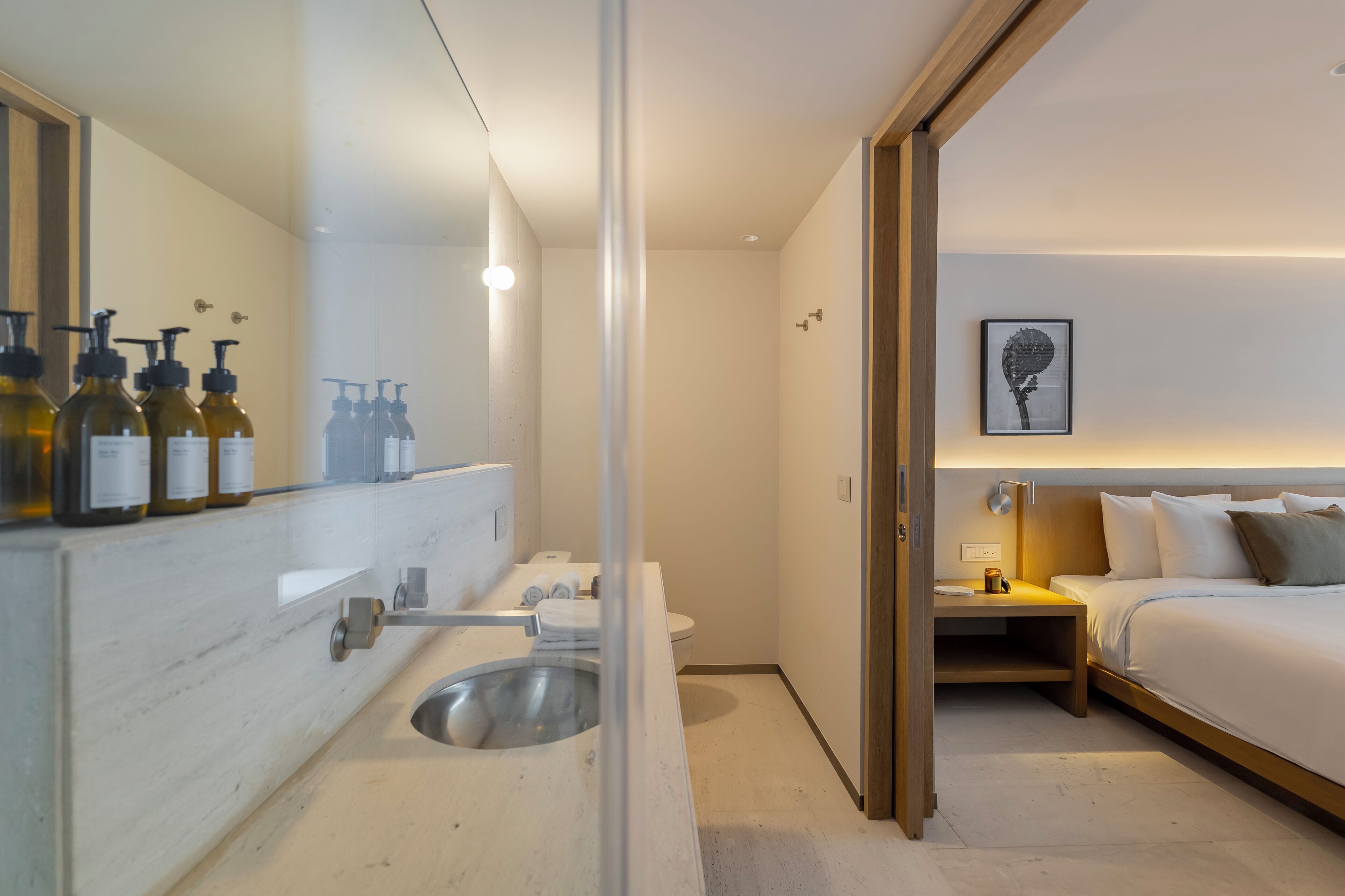 A modern hotel bathroom with a large mirror, a sink, and toiletries.