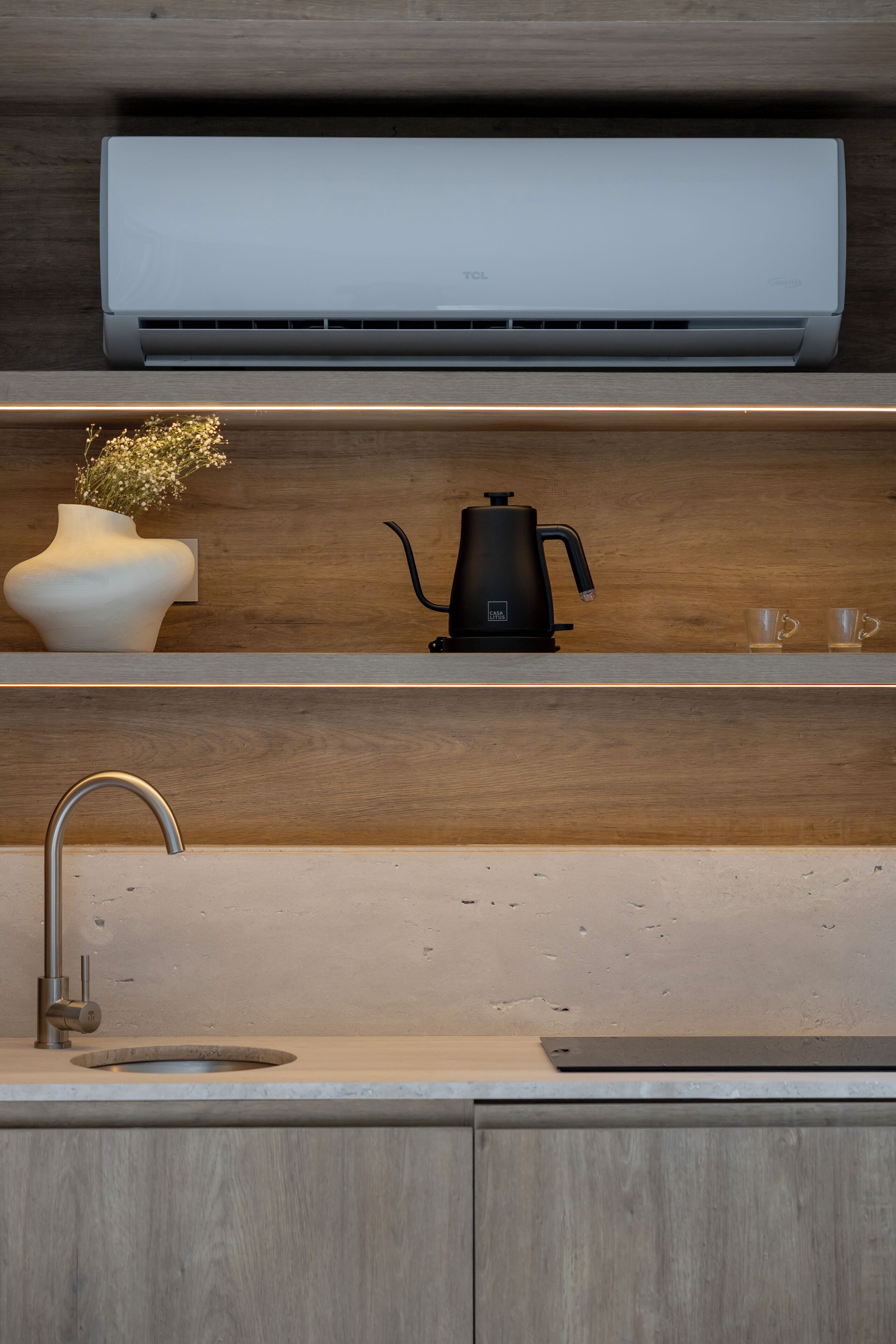 Una cocina moderna con aire acondicionado integrado, cafetera, un jarrón con flores y un lavamanos.