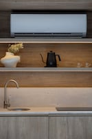A modern kitchen with a built-in air conditioner, a coffee maker, a vase with flowers, and a sink.