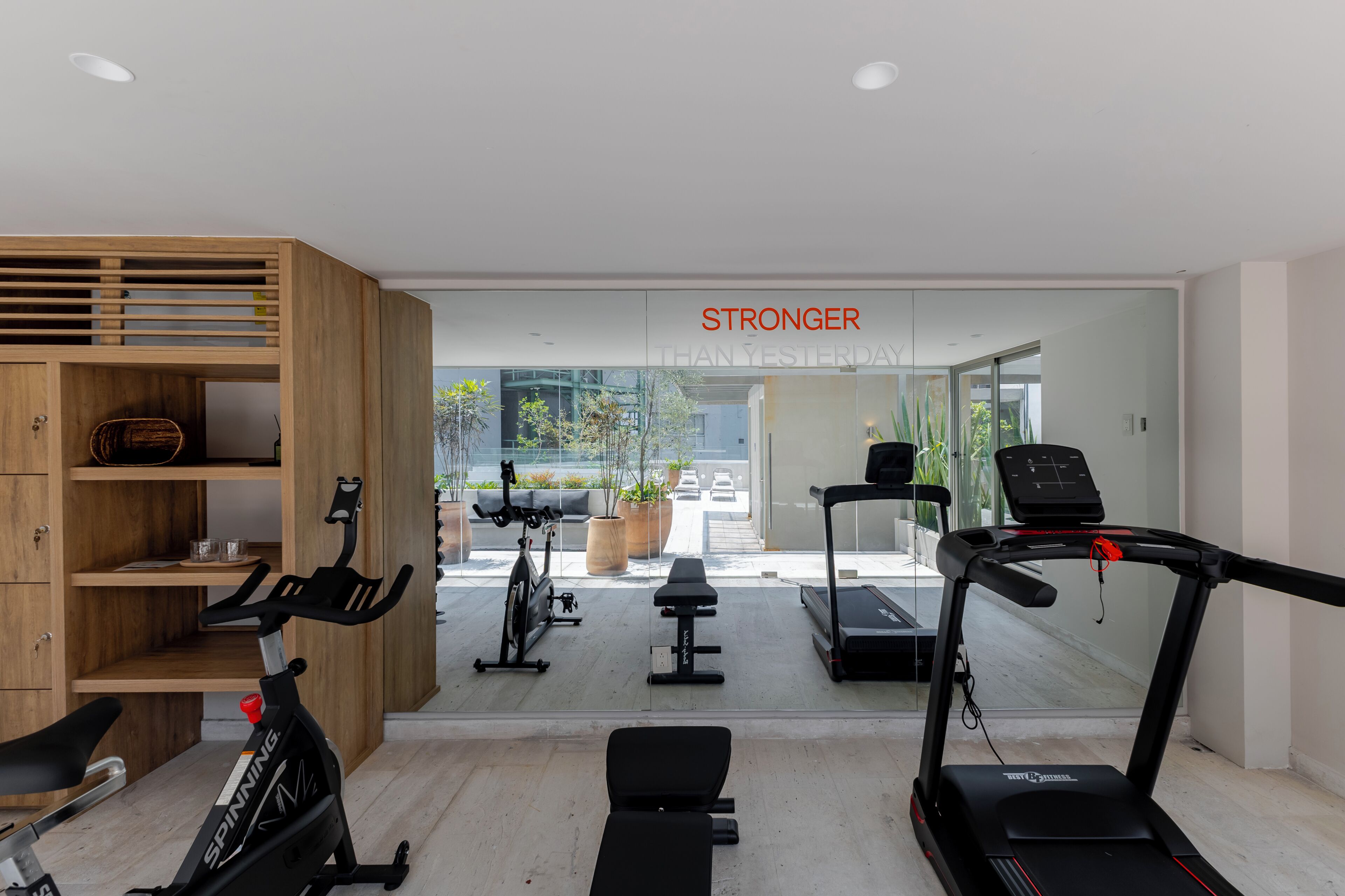 A modern gym with exercise equipment, a wooden cabinet, and a sign that reads 'STRONGER THAN YESTERDAY'.