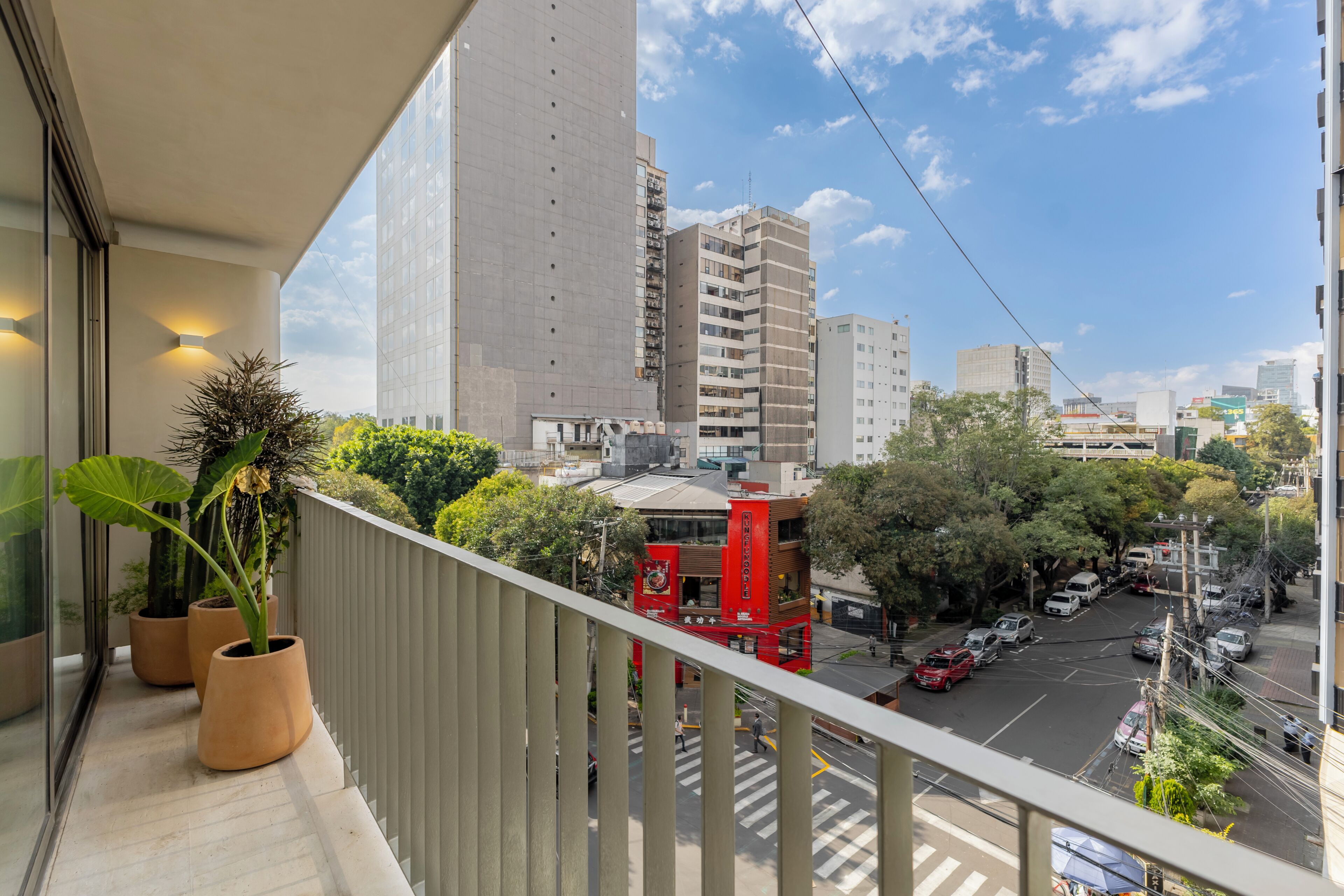 Un balcón con plantas en macetas, vista a una calle y edificios altos.
