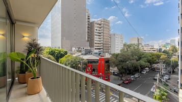 Un balcón con plantas en macetas, vista a una calle y edificios altos.