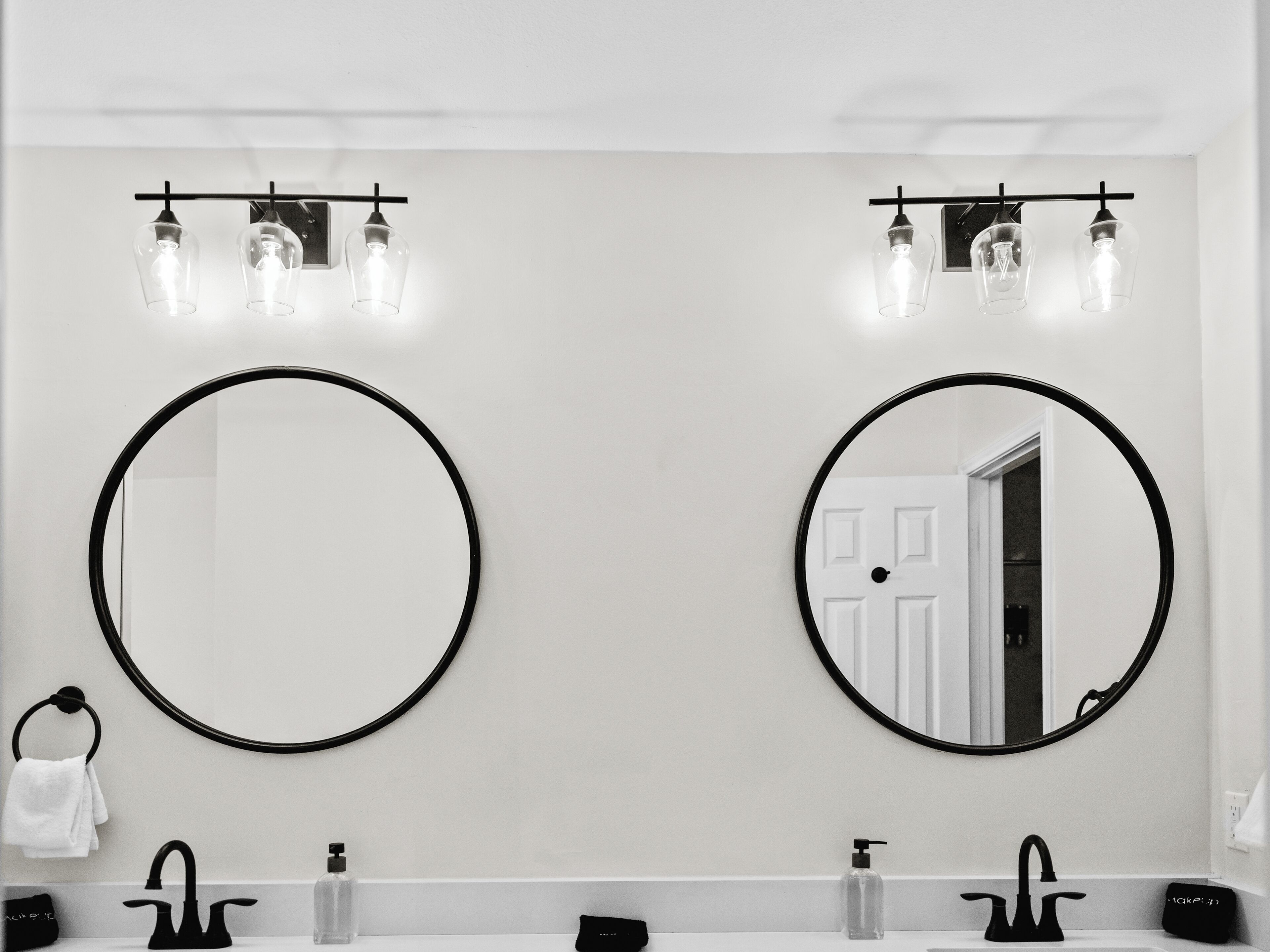 A bathroom with two round mirrors, a towel rack, and a double sink with black faucets.