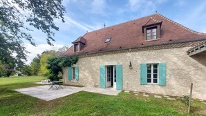 A stone house with a red tiled roof, green shutters, and a small garden area with a table and chairs. - Lovely home in Saint-Aubin-de-Cadelec with WiFi (Saint-Aubin-de-Cadelec)
