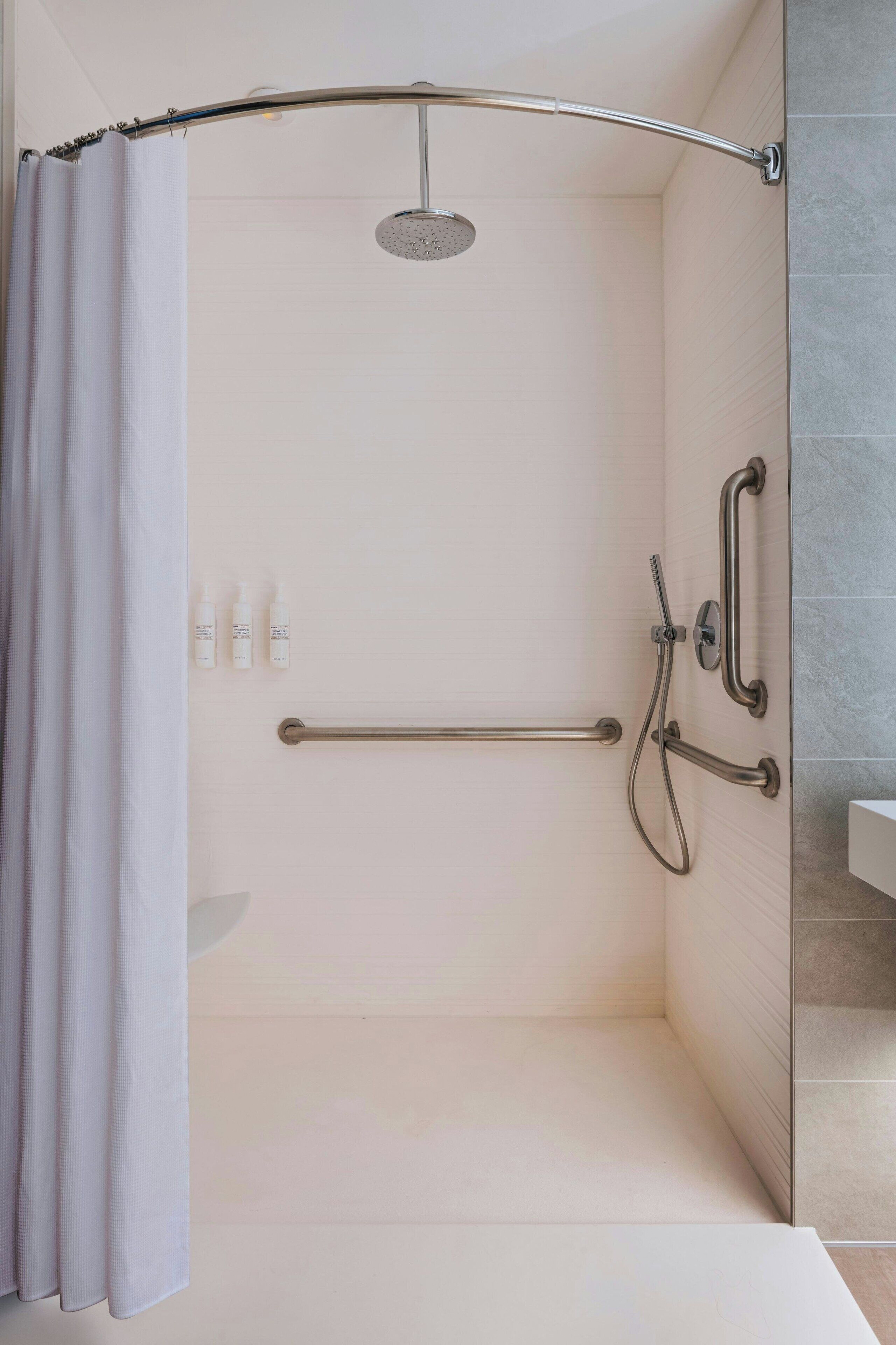 A walk-in shower with a curved showerhead, grab bars, and a towel rack.