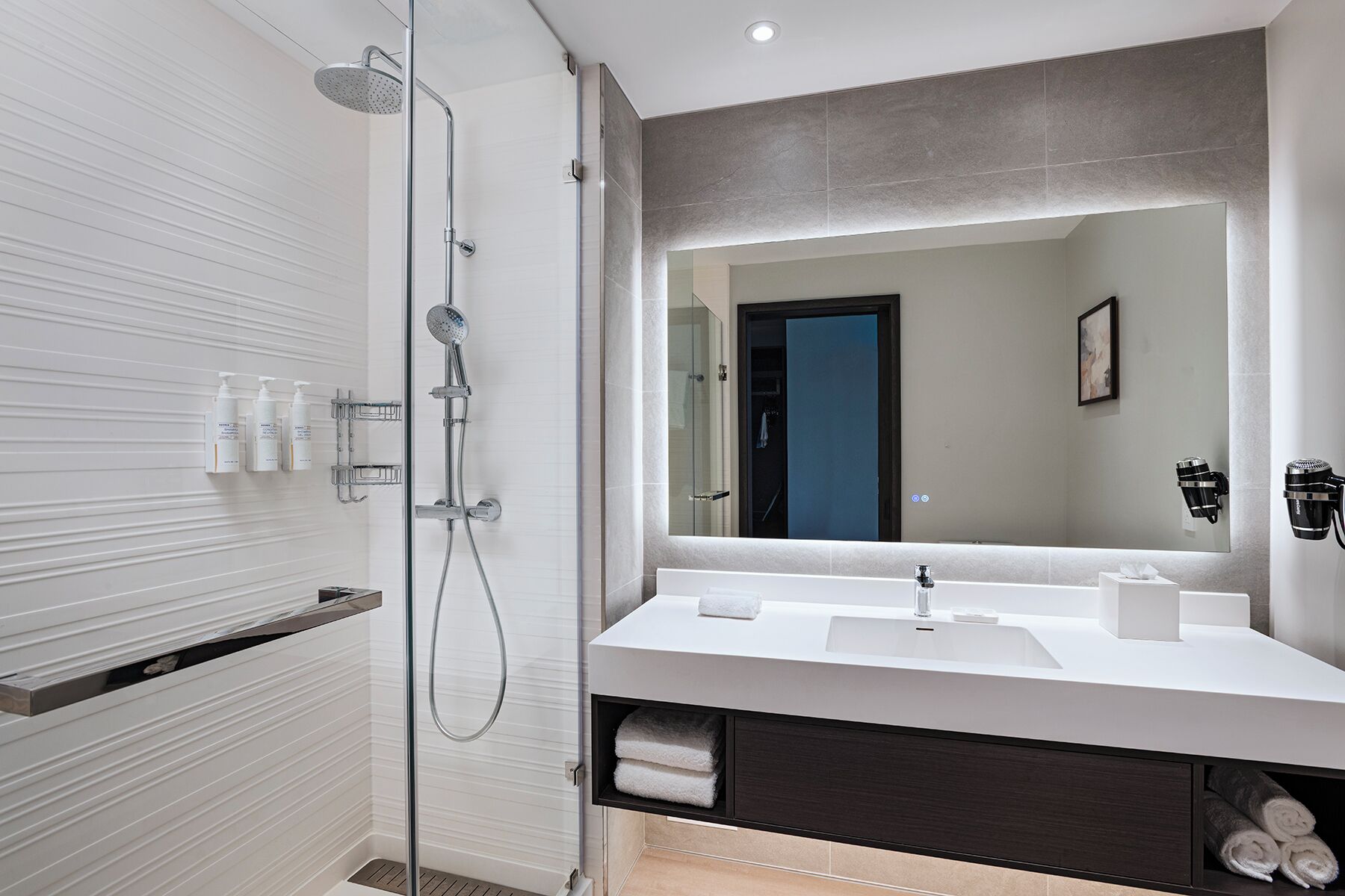 Un baño moderno con ducha envuelta en vidrio, un espejo grande y un mueble de tocador con lavabo y barra para toallas.