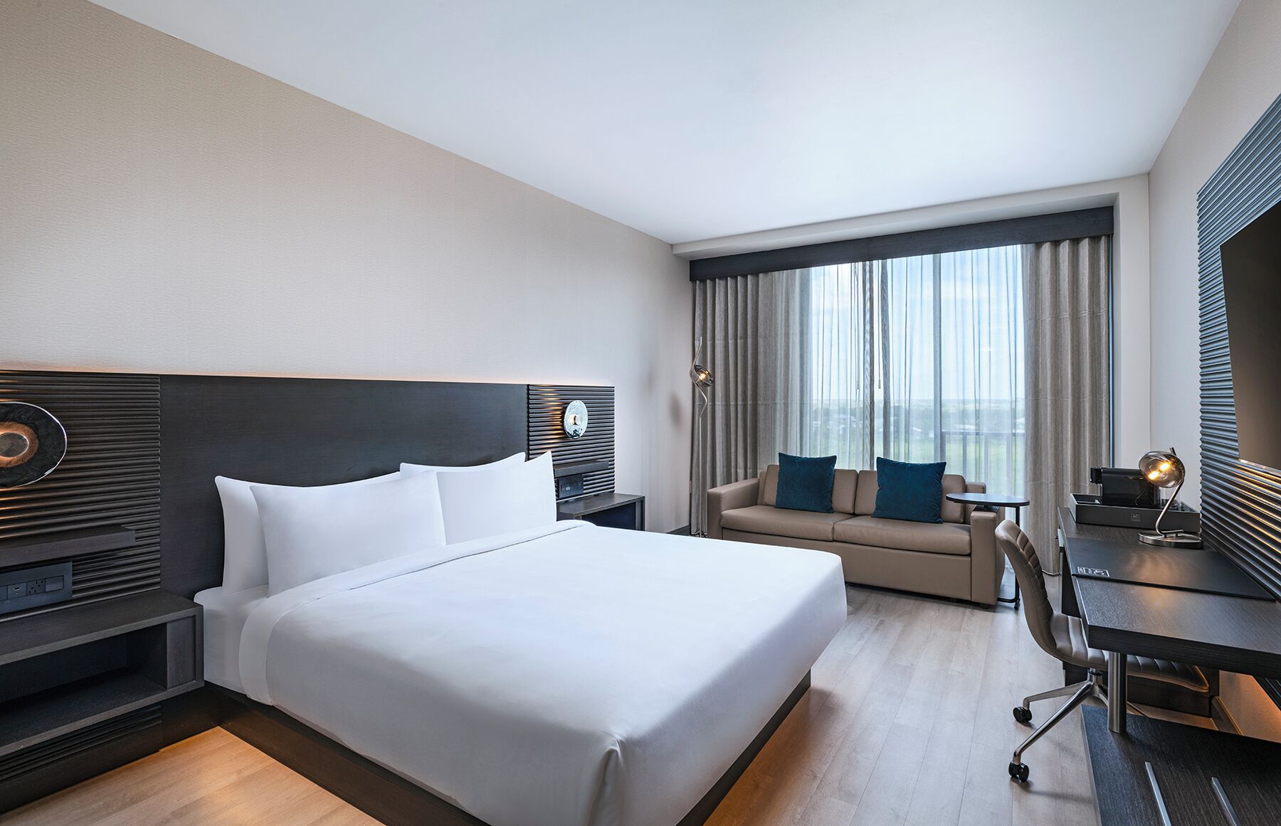 Quarto de hotel com uma cama grande, um sofá, uma escrivaninha e vista para a cidade.
