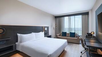 Quarto de hotel com uma cama grande, um sofá, uma escrivaninha e vista para a cidade.
