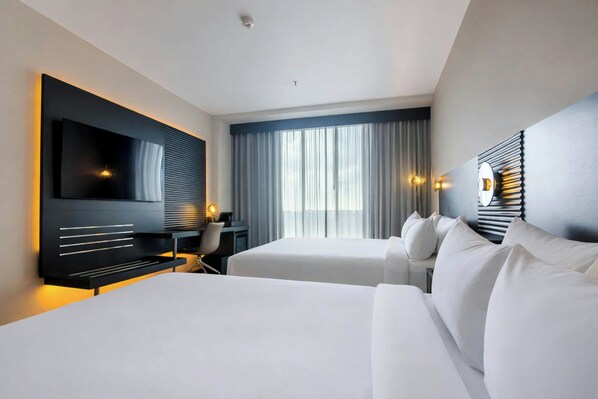 A hotel room with a large flat-screen TV, two beds, a desk, and a chair. - AC Hotel Georgetown Guyana (Georgetown)