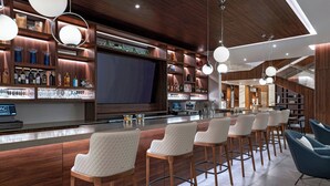 A modern bar area with wooden shelves, bar stools, and a large flat-screen TV. - AC Hotel Georgetown Guyana (Georgetown)