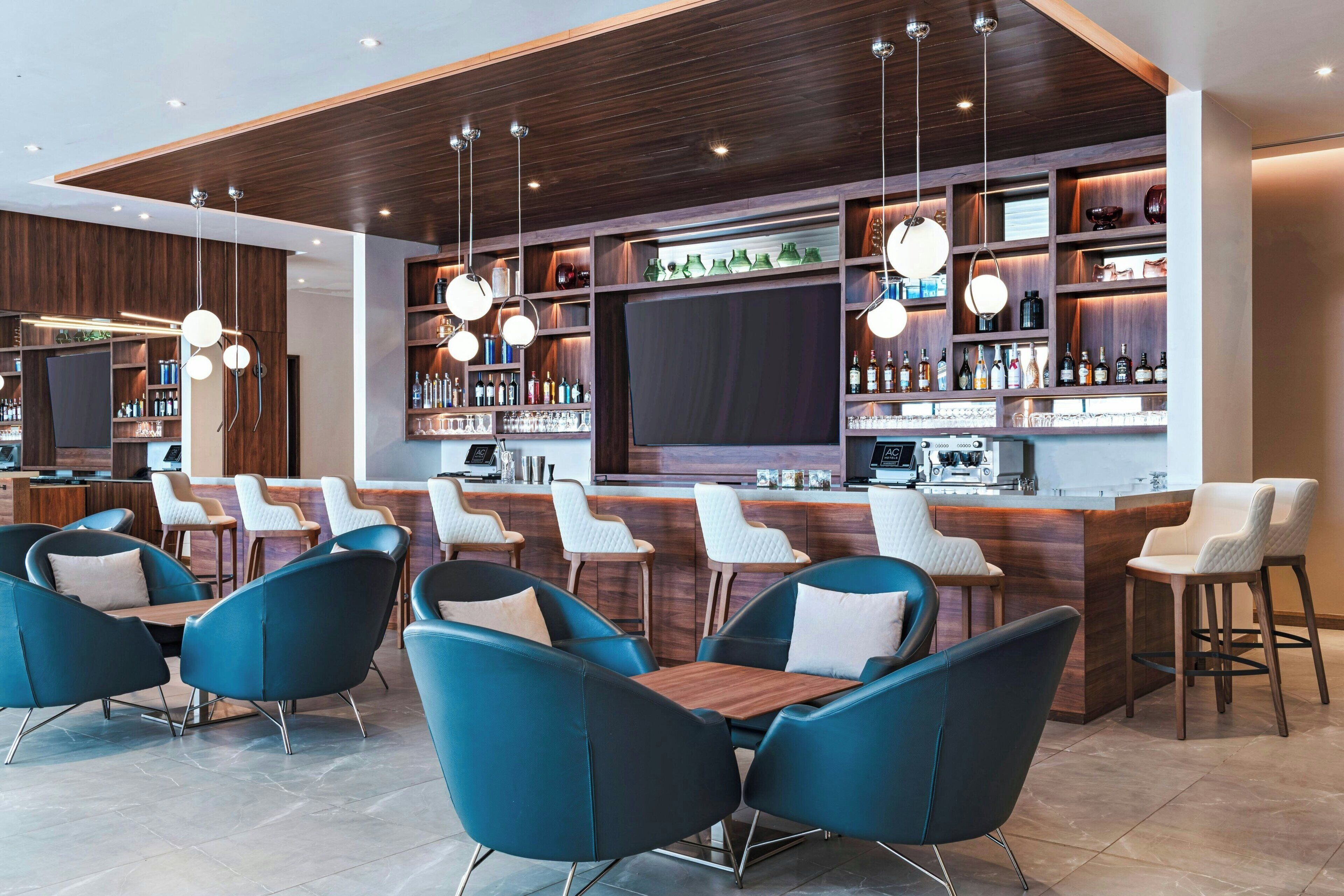 Uma área de bar moderna com cadeiras azuis, balcão de madeira e prateleiras cheias de garrafas.