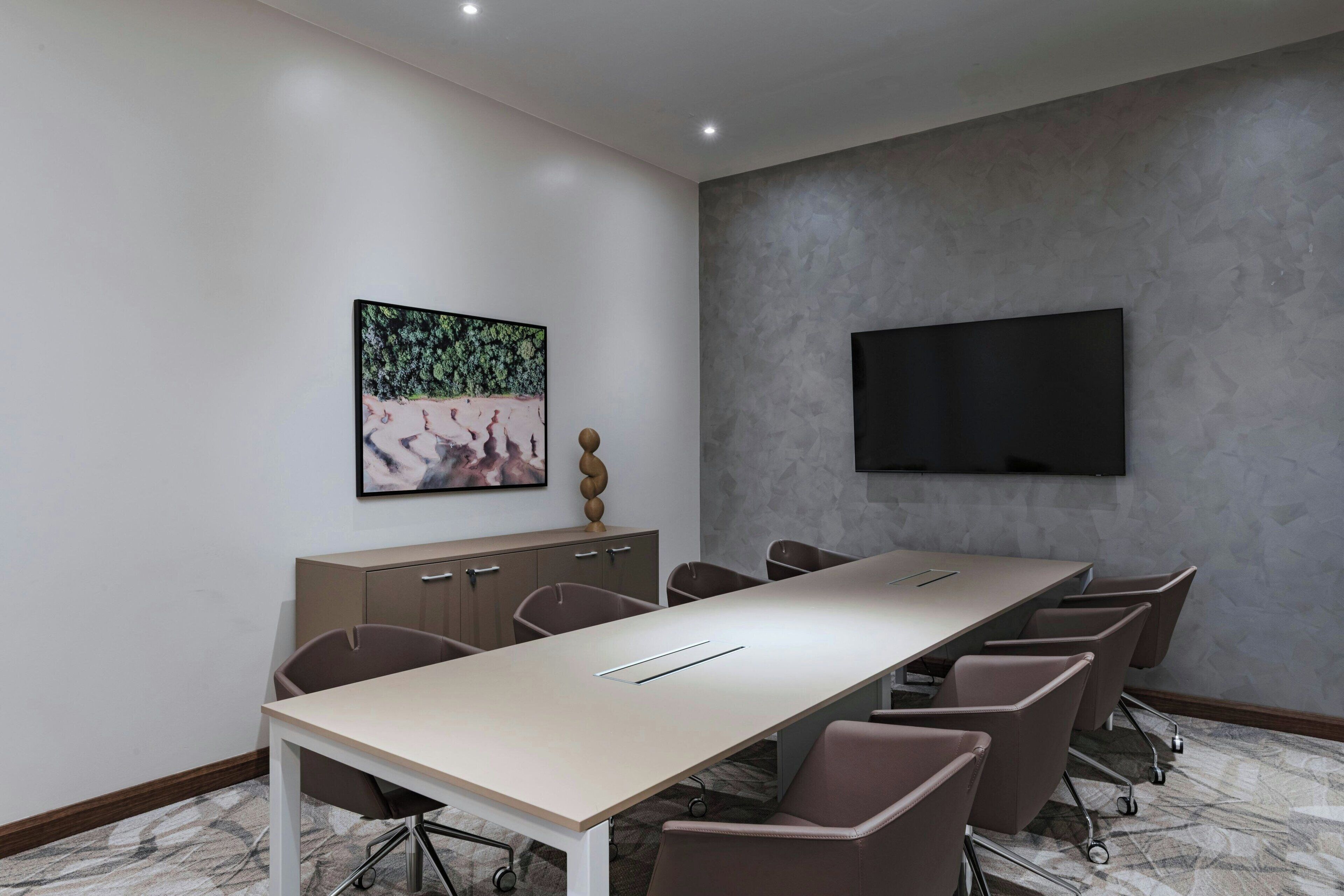 A conference room with a long table, chairs, a TV, and a cabinet with drawers.