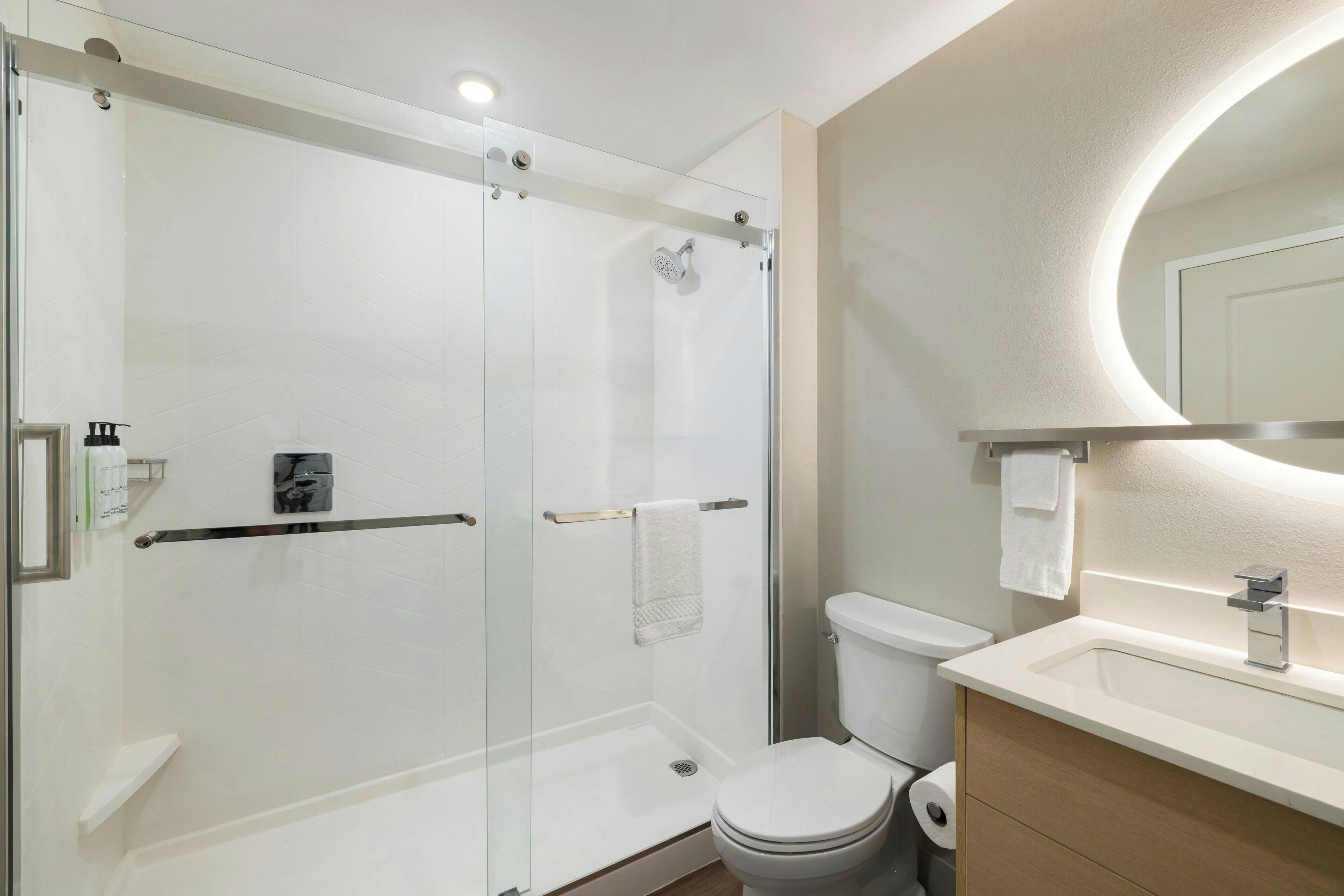 A modern bathroom with a glass-enclosed shower, a toilet, and a sink with a mirror above it.