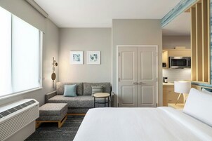 Habitación de hotel con cama, sofá, mesita pequeña, microondas y acceso a la cocina.