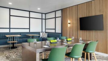 A conference room with a long table, green chairs, a blue sofa, and a flat-screen TV mounted on the wall.