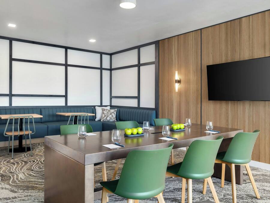 A conference room with a long table, green chairs, a blue sofa, and a flat-screen TV mounted on the wall.