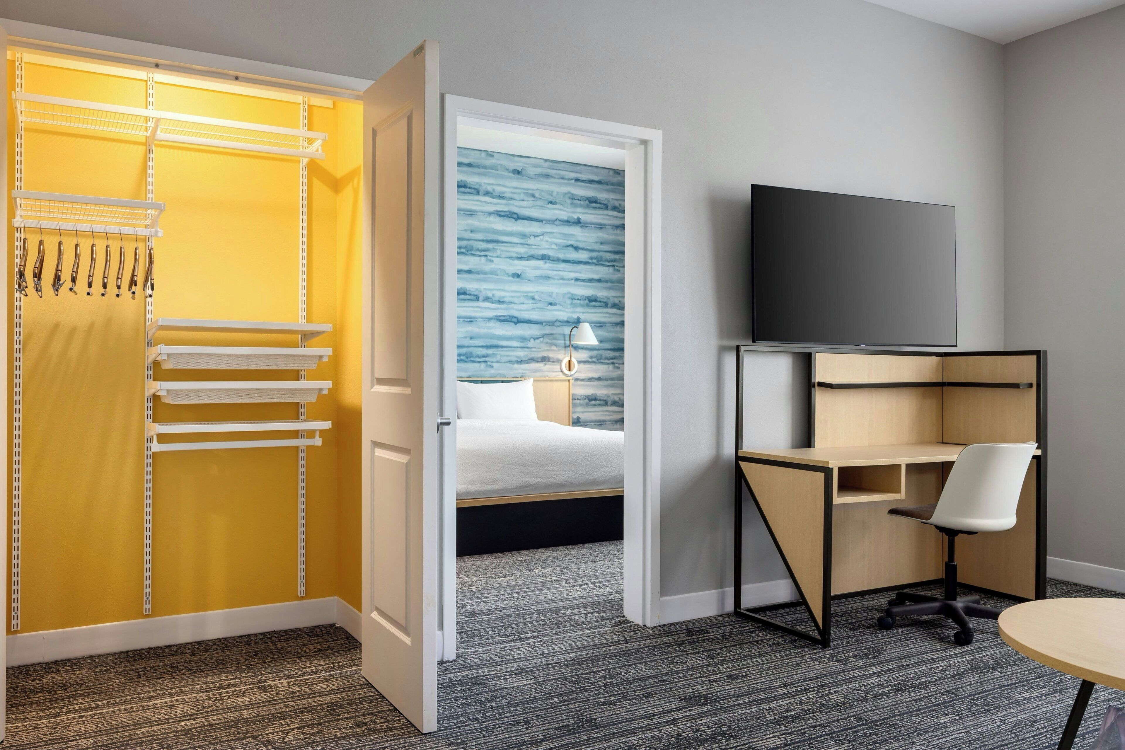 Een hotelkamer met een gele kast, een bed tegen een blauwe muur, een bureau met stoel, en een televisie.
