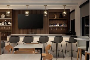 A modern bar area with a flat-screen TV, wooden shelves with bottles, and bar stools.