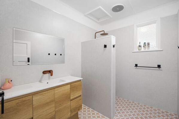 A bathroom with a wooden vanity, a mirror, a shower enclosure, and a window with toiletries. - Salt Soul South Freo - 3BR (Perth)