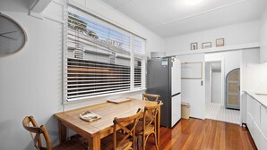 A compact kitchen with a dining area, featuring a wooden table, wicker chairs, a refrigerator, and a window with blinds. - Salt Soul South Freo - 3BR (Perth)