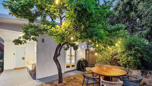A patio with a round wooden table and wicker chairs, surrounded by a brick floor and a white wall. - Salt Soul South Freo - 3BR (Perth)