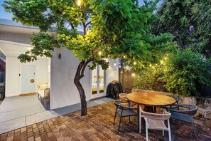 A patio with a round wooden table and wicker chairs, surrounded by a brick floor and a white wall. - Salt Soul South Freo - 3BR (Perth)