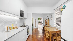 A compact kitchen with white cabinets, a wooden dining table, and a view into the backyard. - Salt Soul South Freo - 3BR (Perth)