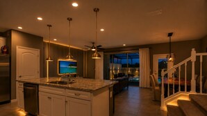 Une cuisine moderne dotée d’un îlot central, de luminaires suspendus et offrant une vue sur l’espace piscine.