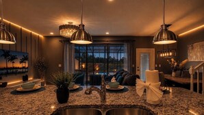 Une cuisine moderne dotée de plans de travail en granit, d’éviers en acier inoxydable, de luminaires suspendus et offrant une vue sur l’extérieur.