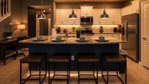 Une cuisine moderne dotée d’un îlot central, de tabourets de bar, de luminaires suspendus et d’appareils électroménagers en acier inoxydable.