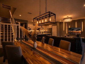 A modern kitchen with a central island, a dining area with a wooden table and chairs, and a staircase leading to another level. - Private Pool 5BR Solterra Retreat by Disney (Davenport)
