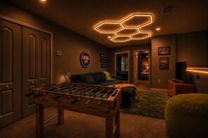 Una habitación acogedora con una mesa de fútbol de mesa, un sofá, un televisor y una pared con un letrero que dice 'LEVEL UP'.