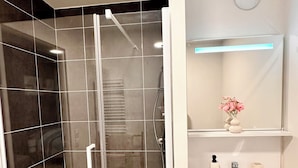 Een moderne badkamer met een douchecabine van glas, een witte wastafel en een spiegel erboven.