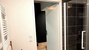 Een moderne badkamer met een douchecabine van glas, een houten handdoekrek en een zichtbare deur naar een andere kamer.