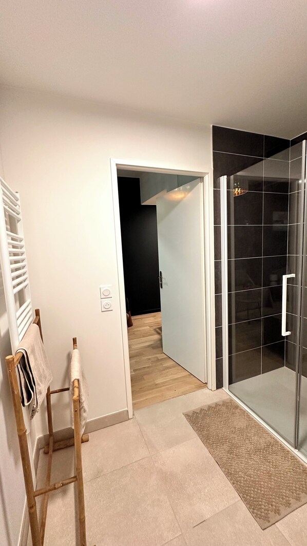 A modern bathroom with a glass shower enclosure, a wooden towel rack, and a visible door leading to another room.