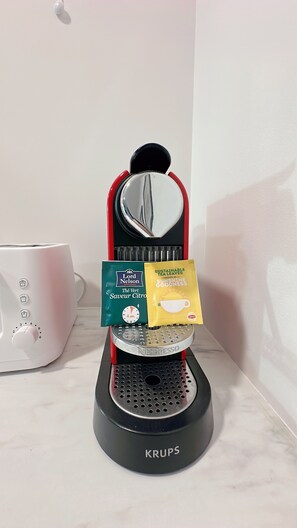A Krups coffee machine with two coffee pods, one green and one yellow, on its drip tray.
