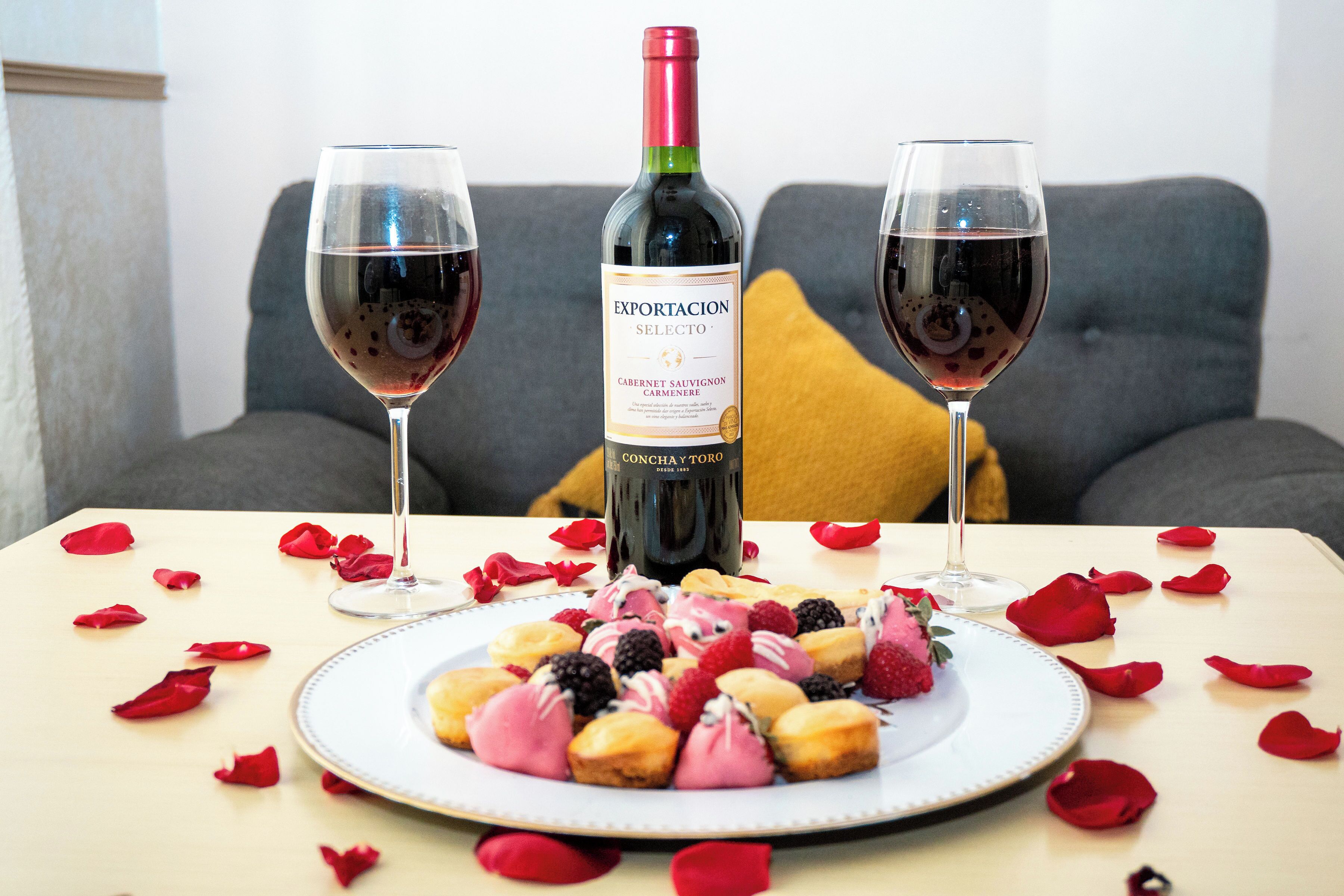 A table with a bottle of wine, two glasses, and a plate of pastries.