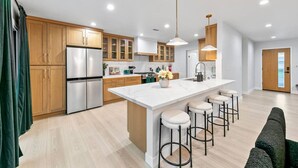 A modern kitchen with wooden cabinets, a stainless steel refrigerator, a marble island with bar stools, and pendant lighting. - Foosball, Hot Tub, Big Backyard, Disneyland, AN12 (Anaheim)