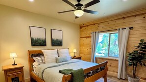 Ein Schlafzimmer mit einem hölzernen Bett, zwei Nachttischen, einem Deckenventilator und einem Fenster mit Vorhängen.