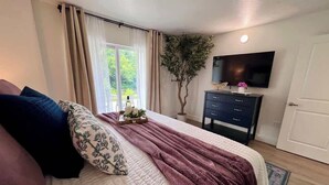 A bedroom with a bed, a dresser, a TV, and a window with curtains. - Floral Cottage by Branson Landing-Waterfront (Branson)