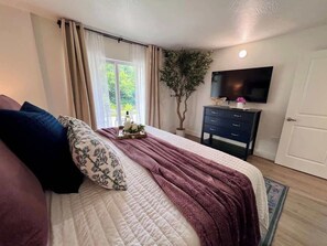 Un dormitorio con cama, cómoda, televisor y ventana con cortinas.