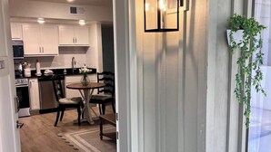 A modern kitchen with white cabinets, a dining area with a round table and chairs, and a hallway leading to a door marked with the number 5. - Floral Cottage by Branson Landing-Waterfront (Branson)