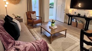 A living room with a sofa, a wooden coffee table, a brown leather chair, a TV, and a door leading outside. - Floral Cottage by Branson Landing-Waterfront (Branson)
