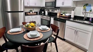 Une cuisine moderne avec des armoires blanches, des appareils en acier inoxydable et un coin repas doté d’une table ronde pour quatre personnes.
