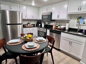 A modern kitchen with white cabinets, stainless steel appliances, and a dining area with a round table set for four.