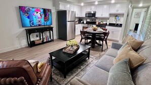 Un salon moderne avec un canapé, une table basse, un téléviseur et une cuisine en arrière-plan.