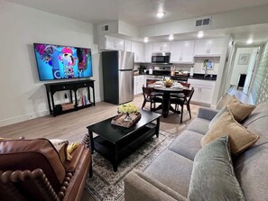 A modern living room with a sofa, coffee table, TV, and a kitchen in the background.