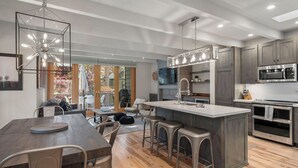 Una cocina moderna con una isla central, electrodomésticos de acero inoxidable y un comedor con mesa de madera y taburetes de bar.